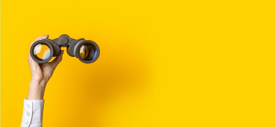 Fernglas mit Hand und gelbem Hintergrund